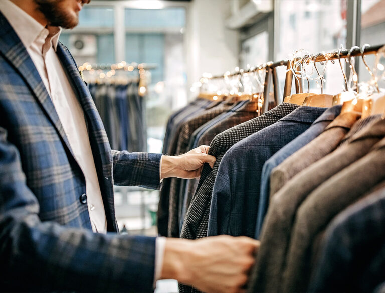 Närbild på en man i blårutig kavaj som bläddrar bland kavajer på en klädställning i butik.