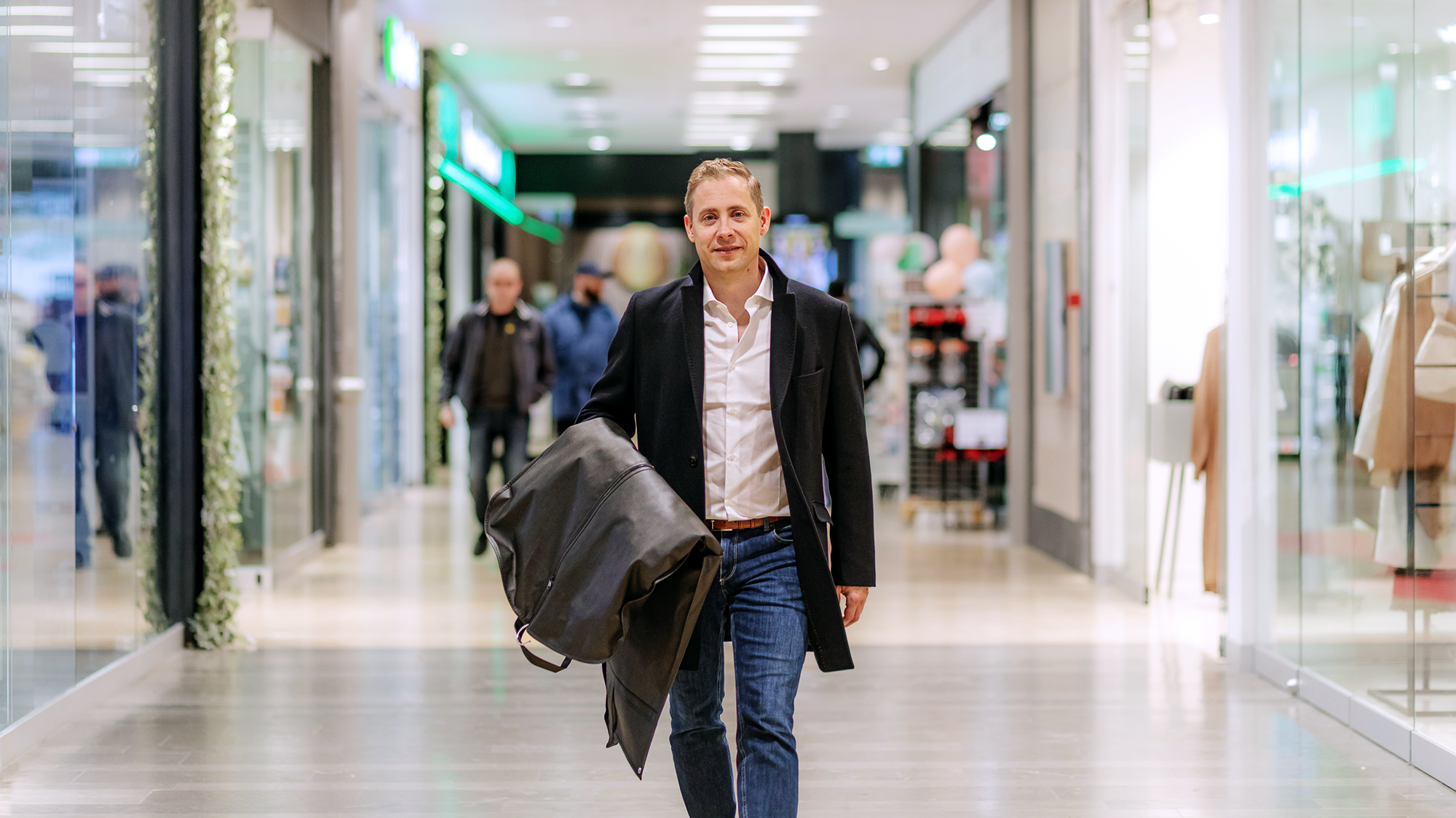Man i svart rock och jeans går genom galleria med stora butiksfönster längst sidorna
