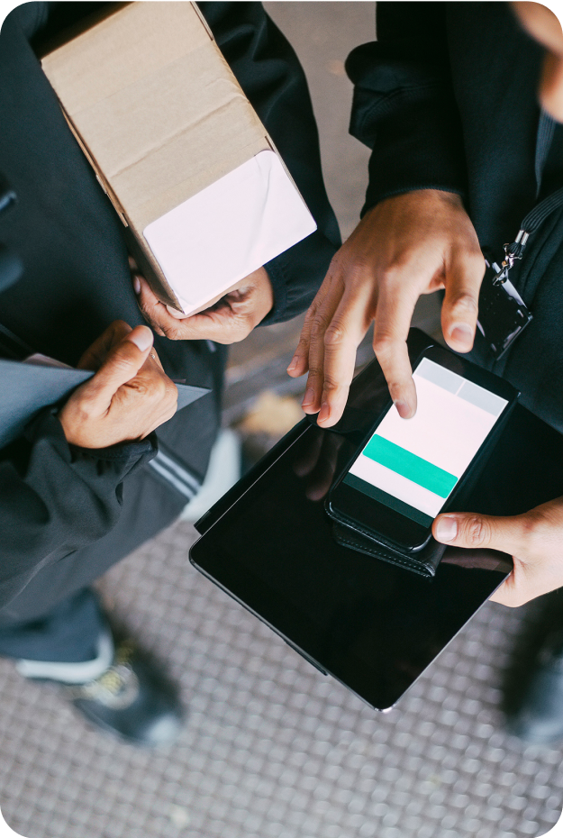 Närbild ovanifrån på två personer i mörka kläder, en använder mobil med Cash IT kassasystem kopplat till visma, den andra håller ett brunt paket