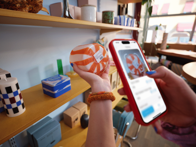 Hand med blåmålade naglar och röd mobil skannar streckkod på orangevit glasprodukt i butikshylla för självskanning med Swish